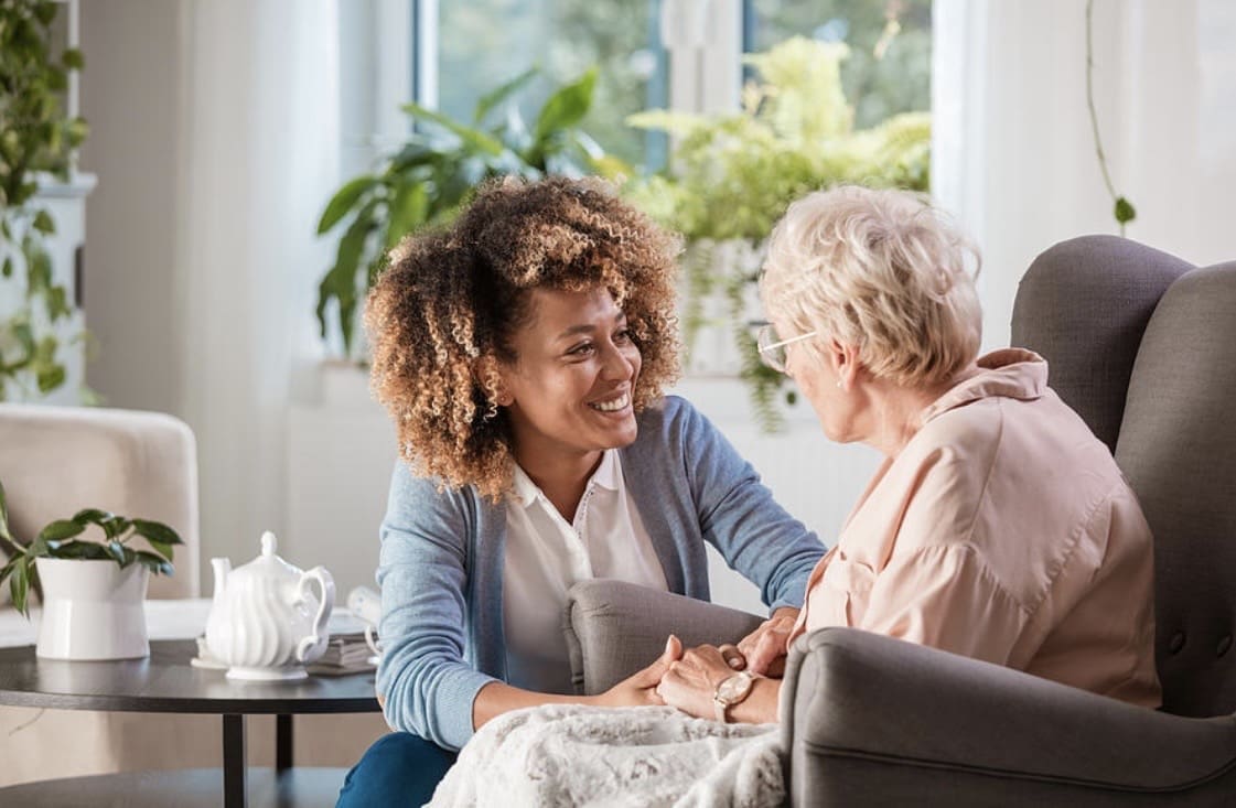 A woman warmly holding an elderly woman's hands during a conversation.